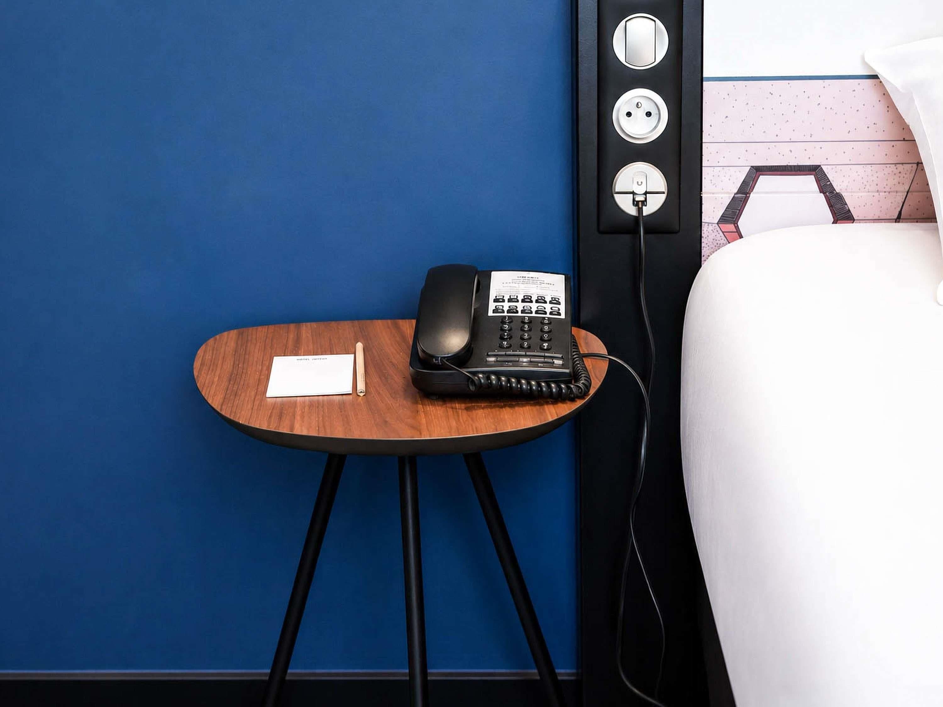 Ein Hotelzimmer mit einem Holznachttisch, einem schwarzen Telefon und einem weißen Kissen.