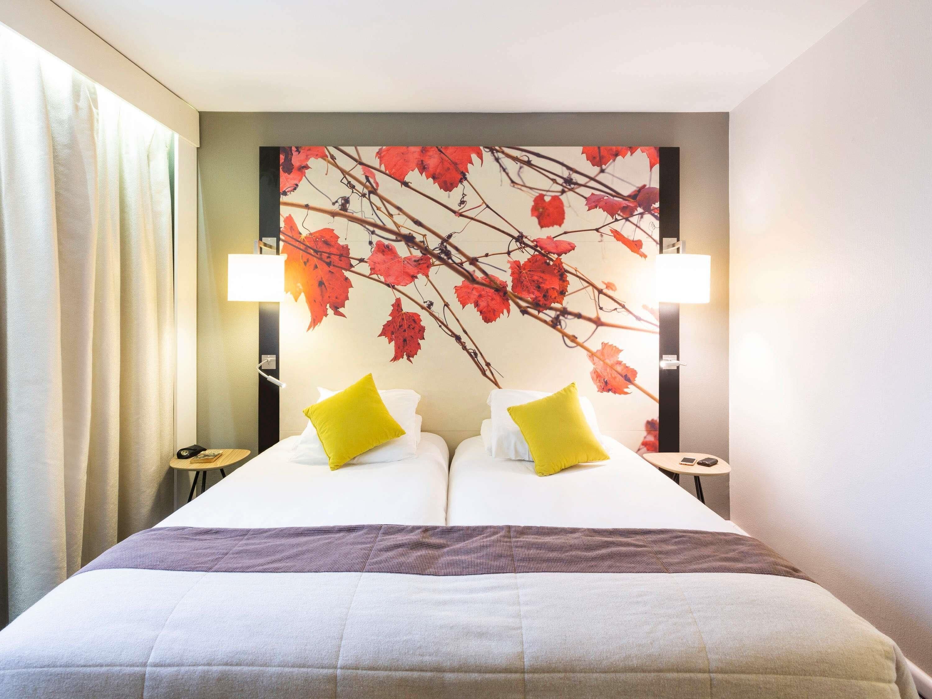 A hotel room with a bed, two bedside lamps, a nightstand, and a wall with a leaf pattern.