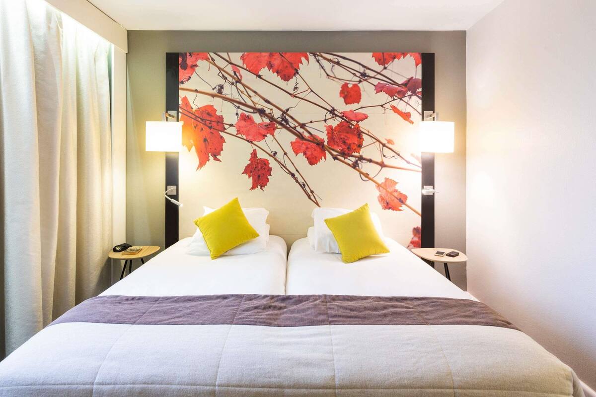 A hotel room with a bed, two bedside lamps, a nightstand, and a wall with a leaf pattern.