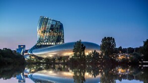 A modern architectural building with a curved glass facade, reflecting on a calm body of water. - Mercure Bordeaux Centre Ville (Bordeaux)