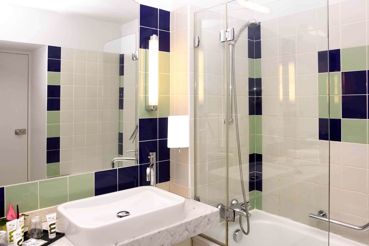 A bathroom with a glass-enclosed shower, a white sink, and a mirror.