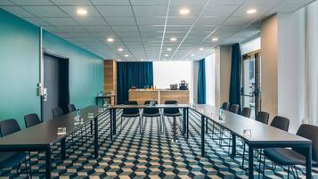 Une salle de conférence équipée d’une longue table, de chaises, d’un projecteur et d’un coin cuisine.