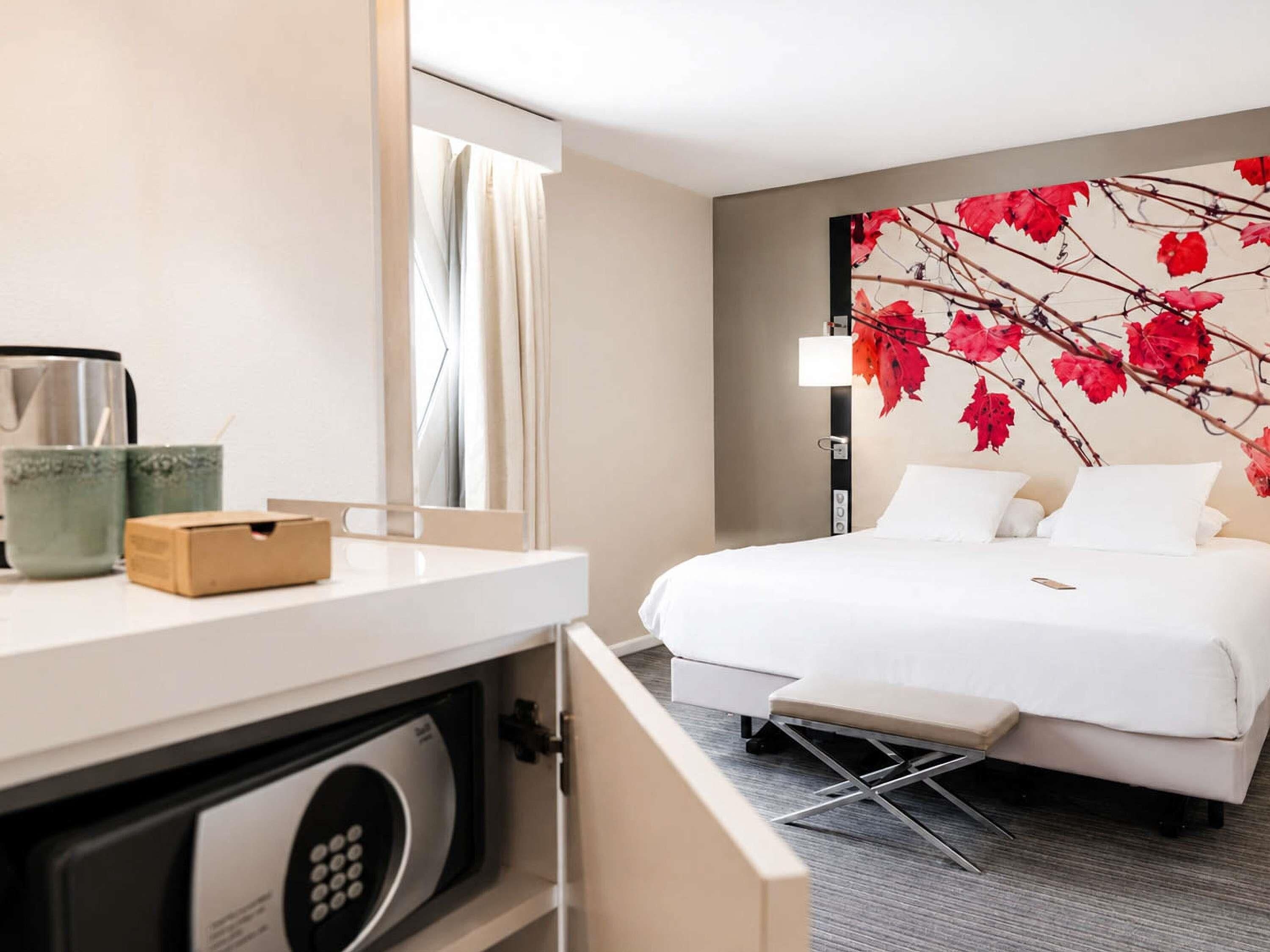 Une chambre d’hôtel avec un lit, un bureau doté d’une machine à café, un four à micro-ondes et un mur orné d’un motif de feuilles rouges.