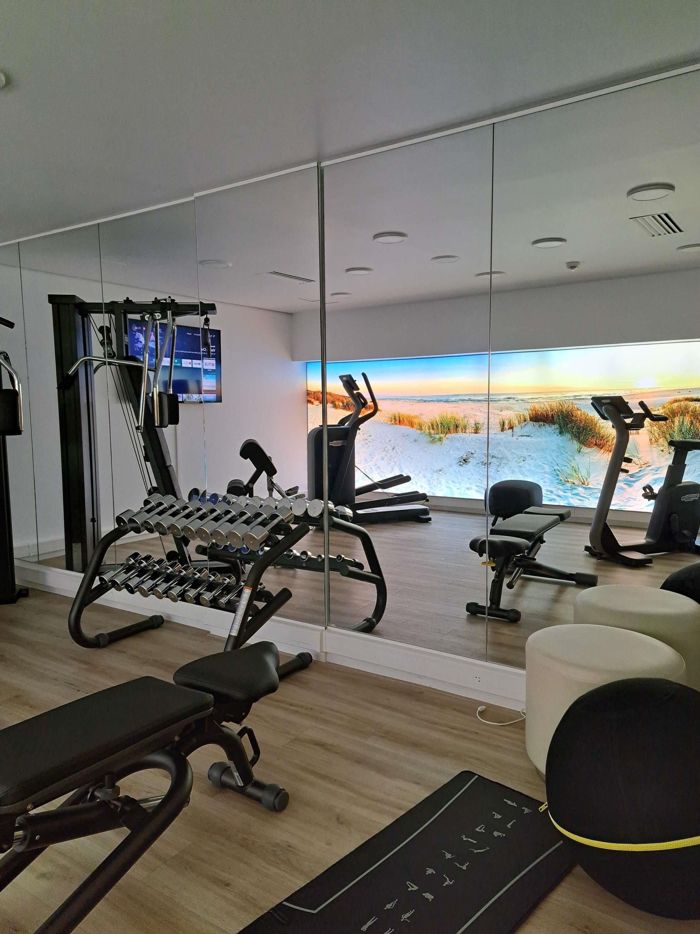 Un gimnasio moderno con equipo de ejercicio, un espejo grande y vistas panorámicas al mar.
