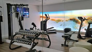 Un gimnasio moderno con equipo de ejercicio, un espejo grande y vistas panorámicas al mar.