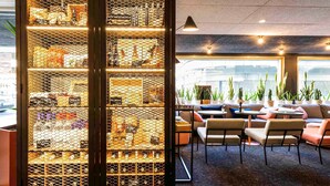 A modern lounge area with a glass partition displaying various items, comfortable seating, and potted plants. - Mercure Bordeaux Centre Ville (Bordeaux)