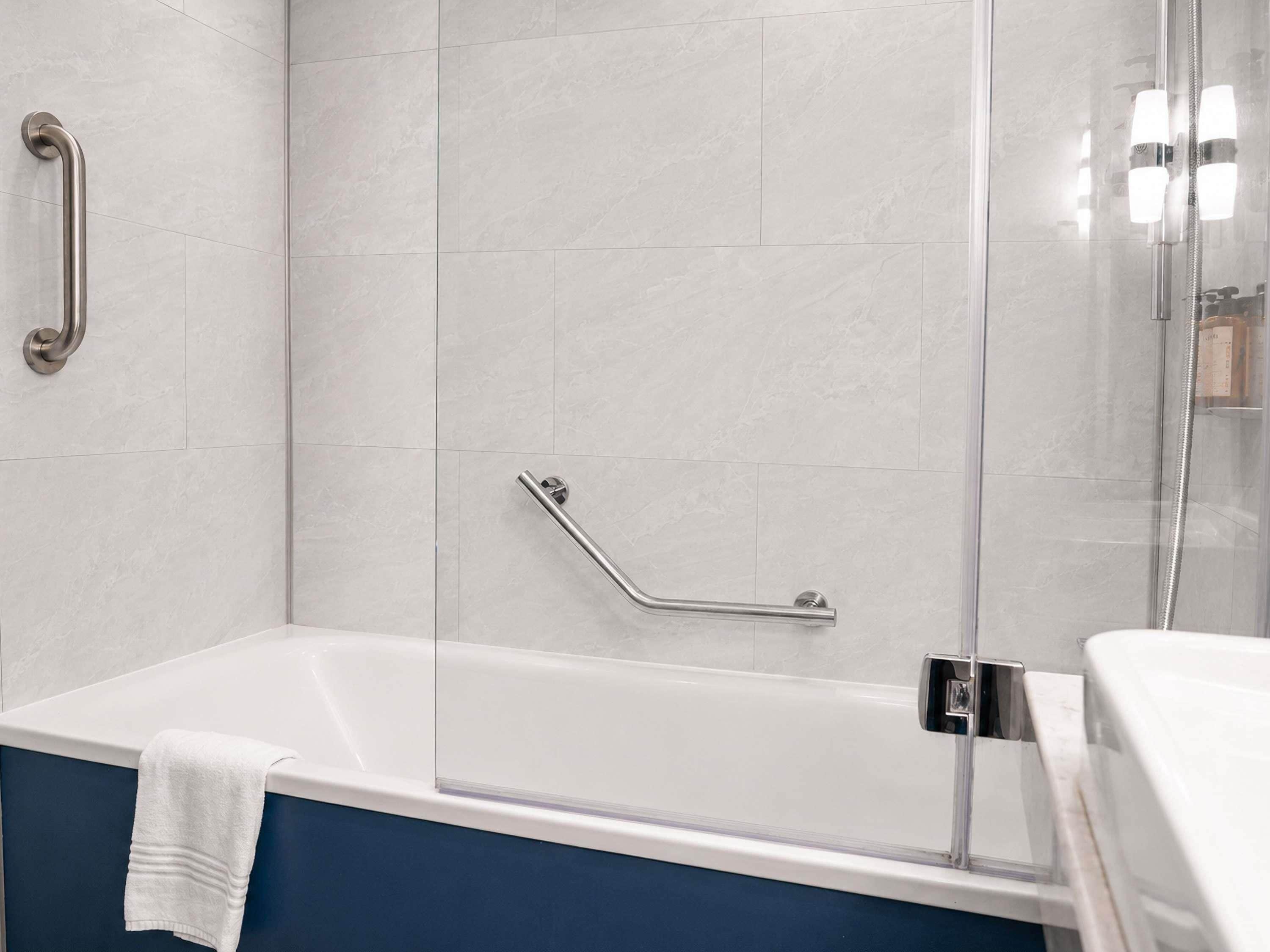 A modern bathroom with a bathtub, a glass shower enclosure, and a handrail.