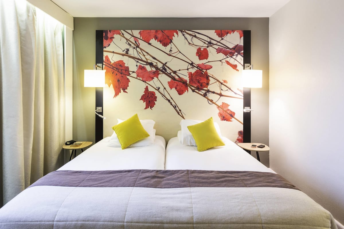 A hotel room with a bed, two pillows, a headboard with a leaf pattern, two bedside lamps, and a nightstand with a phone.
