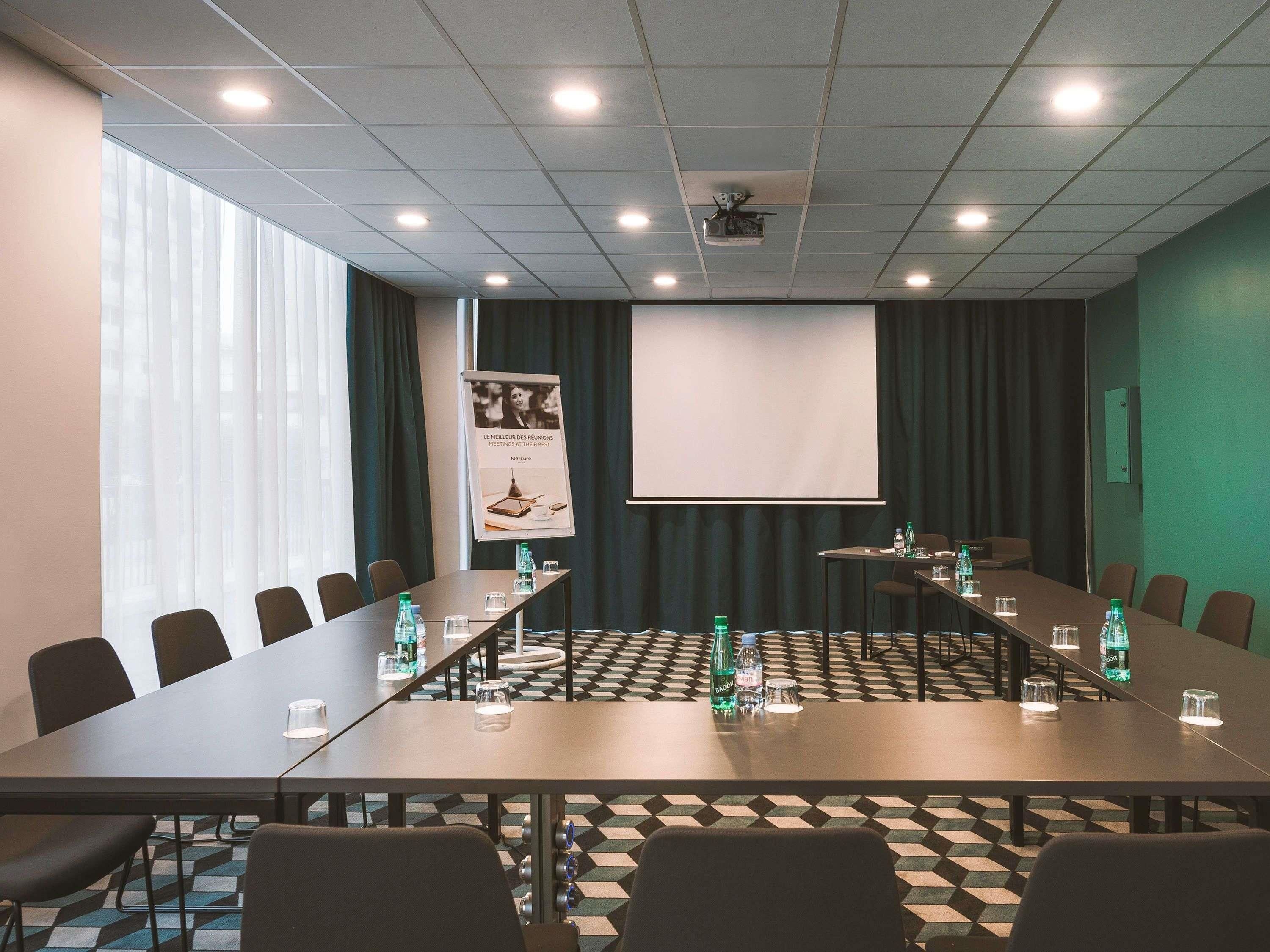 Un salón de conferencias con una larga mesa, sillas, una pantalla de proyector y un cartel.