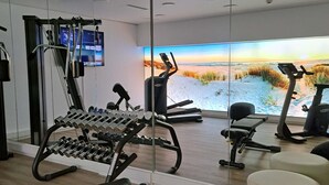 Un gimnasio moderno con equipo de ejercicio, un espejo grande y vistas panorámicas al mar.