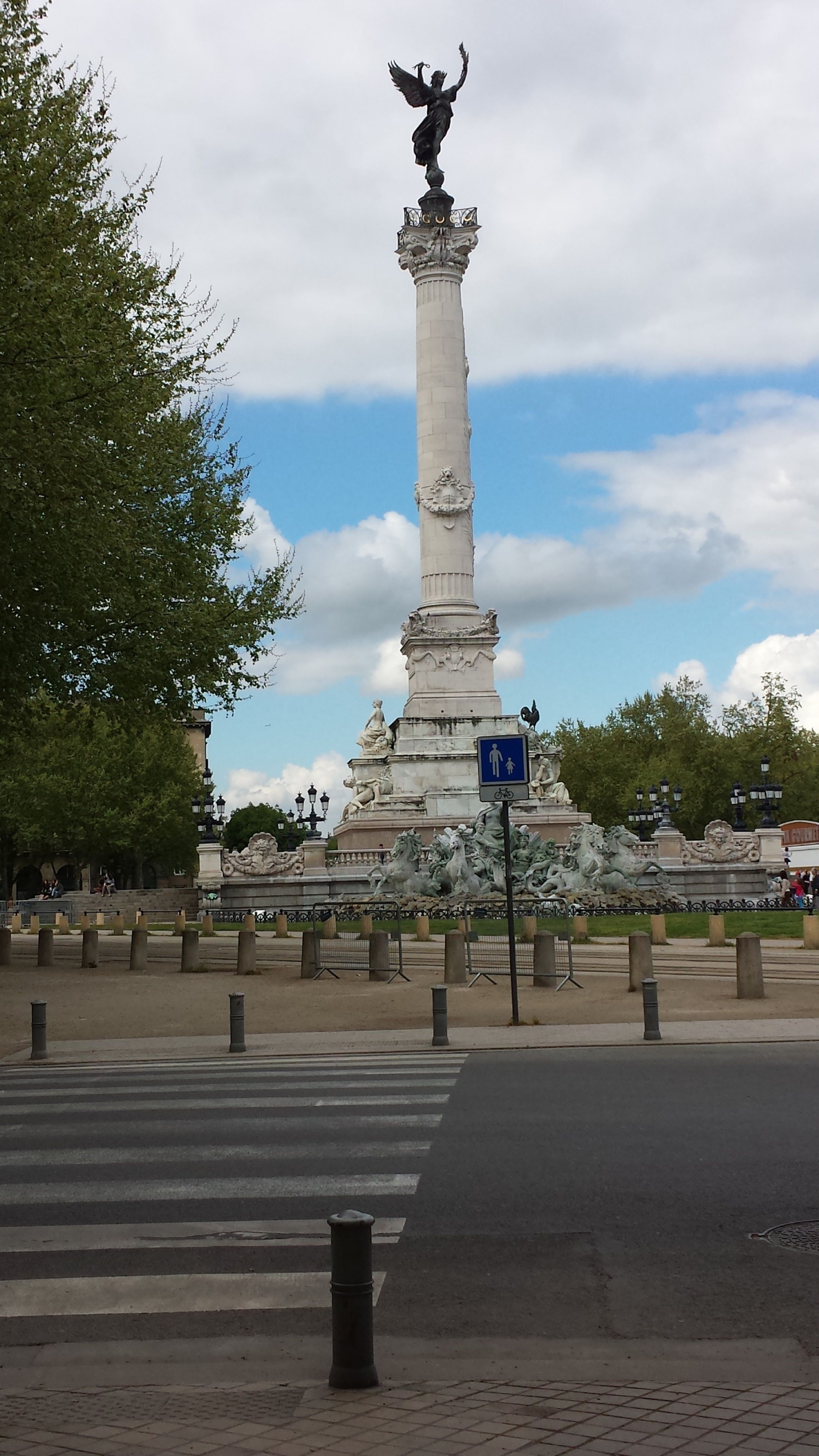 A monument with a statue on top, surrounded by a fence and trees.