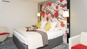 Habitación de hotel con cama, una silla, una mesita pequeña y una pared decorada con un diseño de hojas.