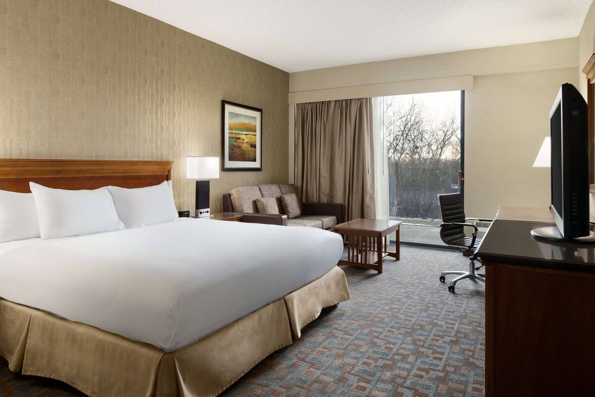 A hotel room with a large bed, a desk, a chair, a sofa, and a window with curtains.