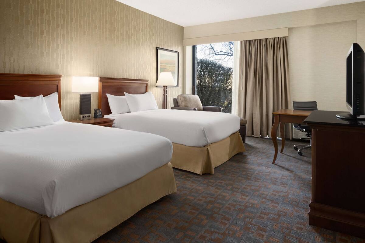 A hotel room with two beds, a desk, a chair, a television, and a window with curtains.
