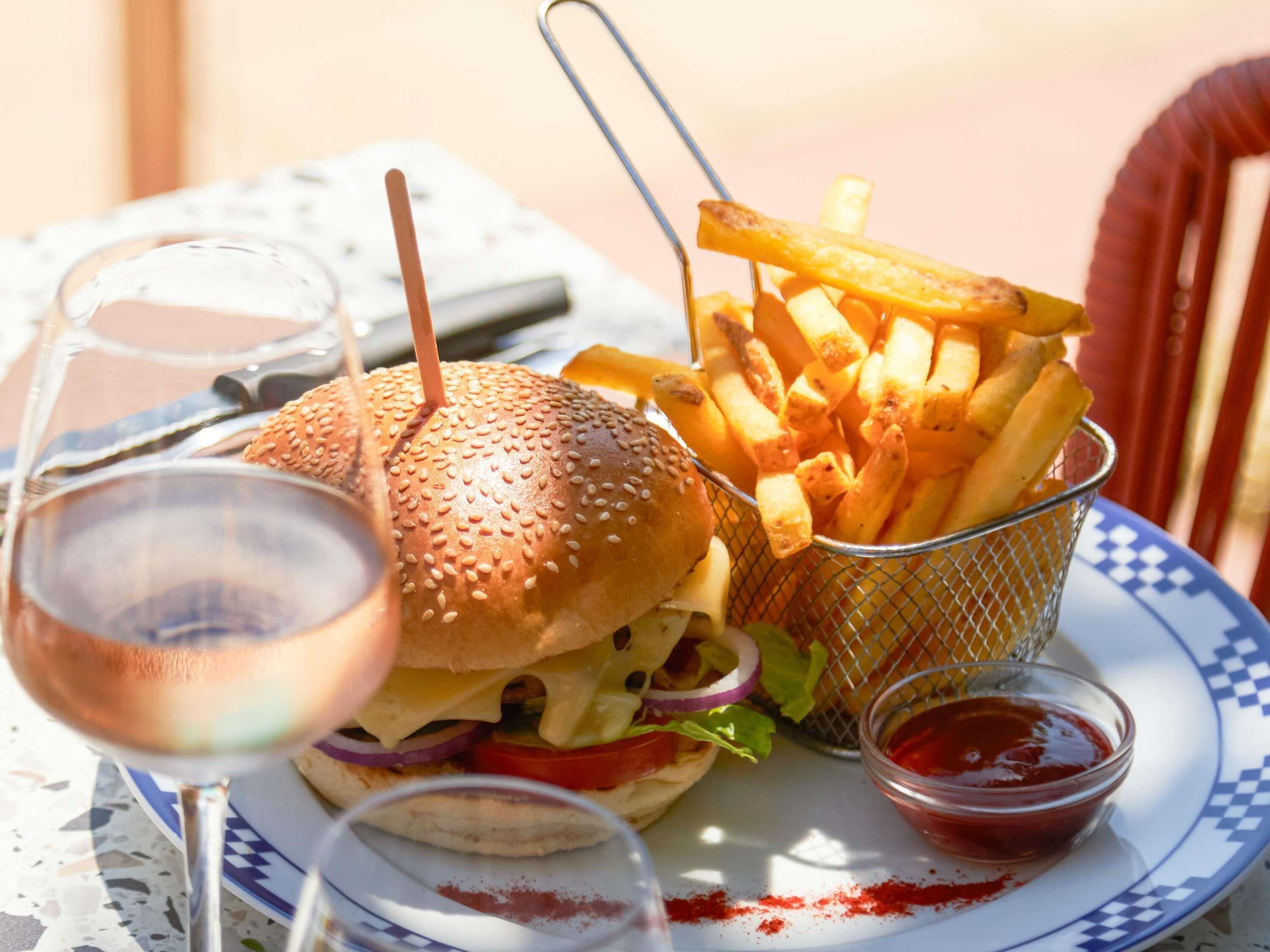 Una comida que incluye una hamburguesa, papas fritas y una bebida, servida sobre una mesa con mantel a cuadros.