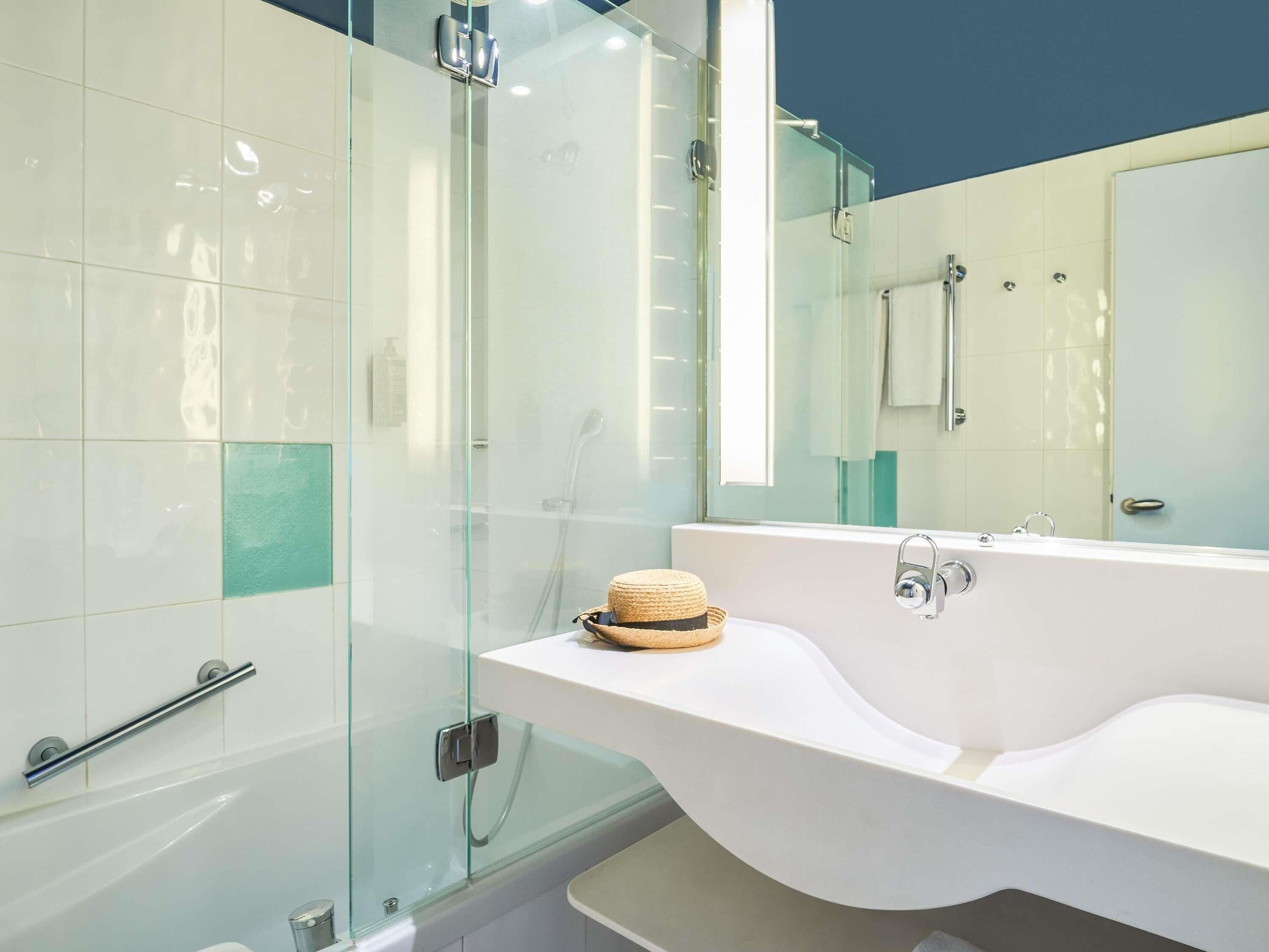 A modern bathroom with a glass shower enclosure, a white sink with a towel, and a large mirror.