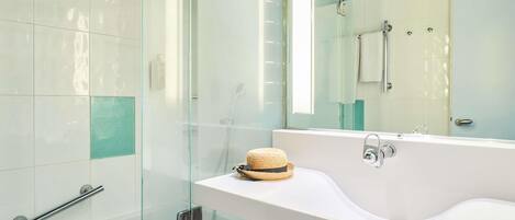 A modern bathroom with a glass shower enclosure, a white sink with a towel, and a large mirror.