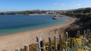 Une plage côtière avec une eau claire, un rivage sablonneux et une clôture en bois au premier plan.