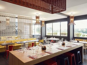 Een restaurant met een lange eettafel, meerdere stoelen en een hoge plafond met hangende lampen.