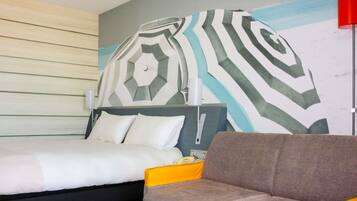 Een hotelkamer met een bed, een slaapbank, een muur met een geometrisch patroon en een rode lamp.