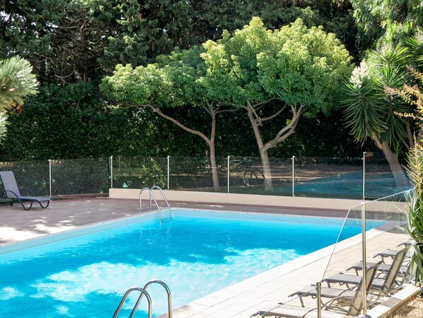 A swimming pool with a metal ladder, surrounded by a fence, and trees in the background.