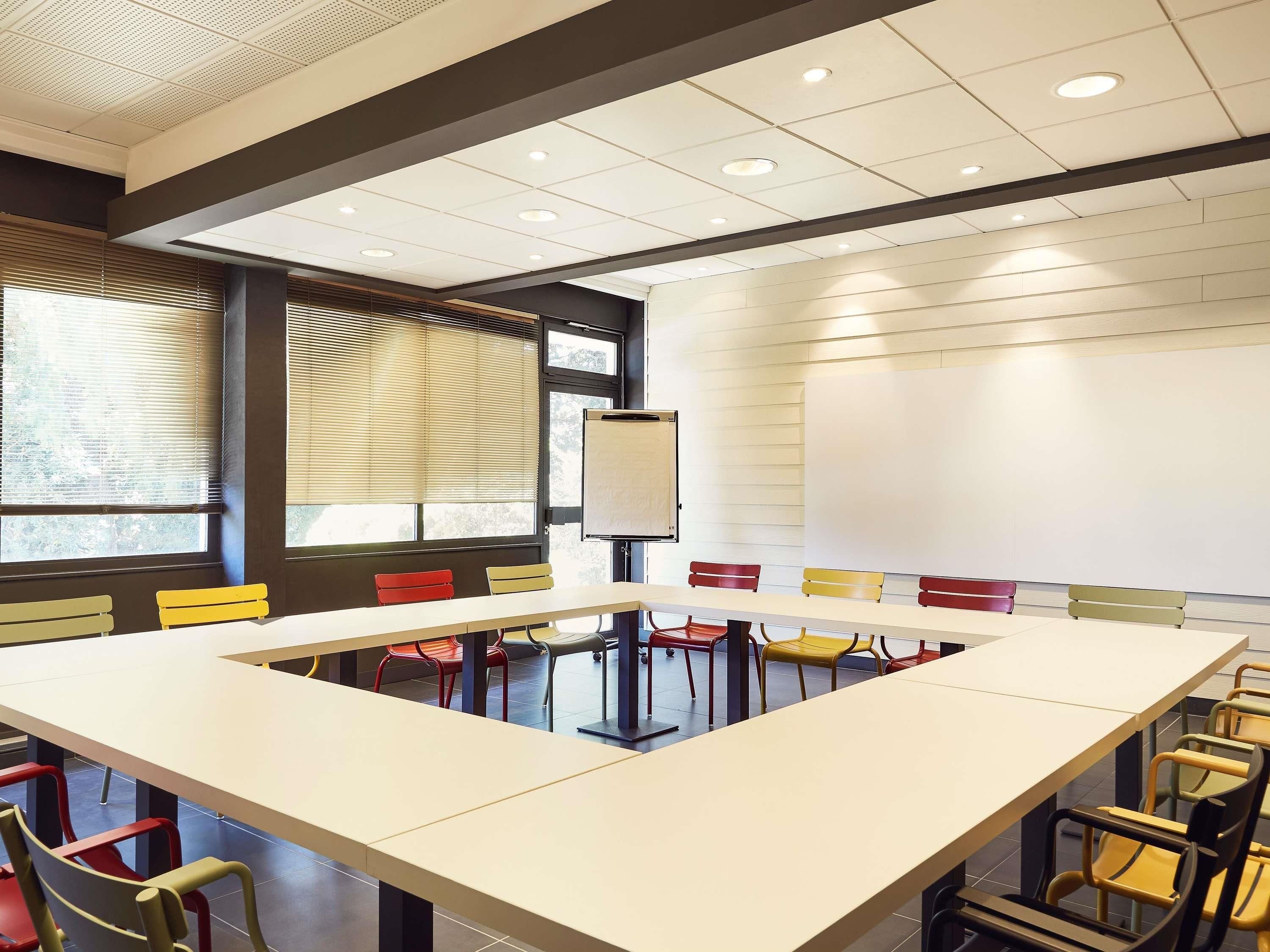 A conference room with a large table, colorful chairs, a whiteboard, and large windows with blinds.