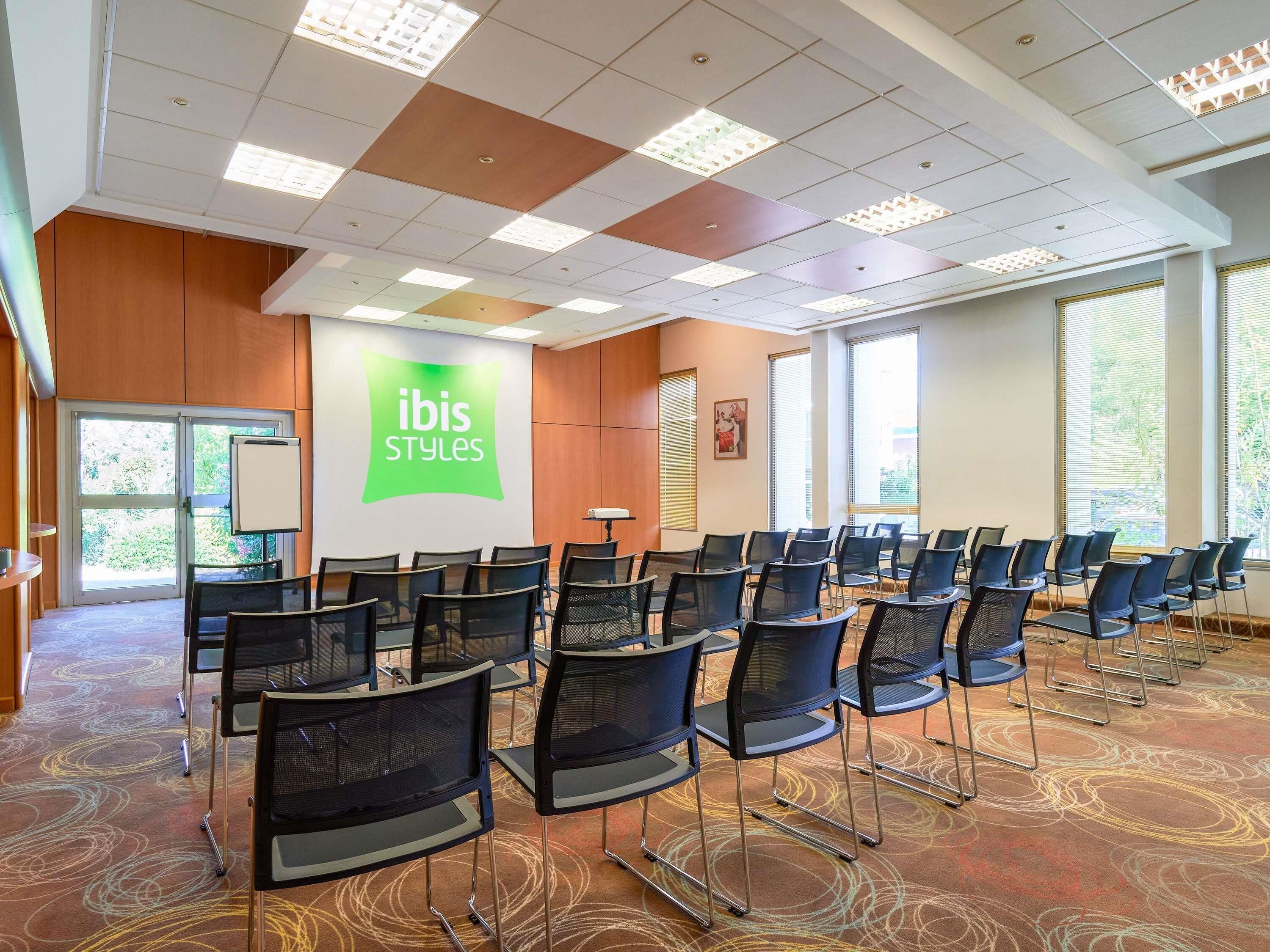 Ein Konferenzraum mit Stuhlreihen, einer Projektionsleinwand und einem großen Fenster.