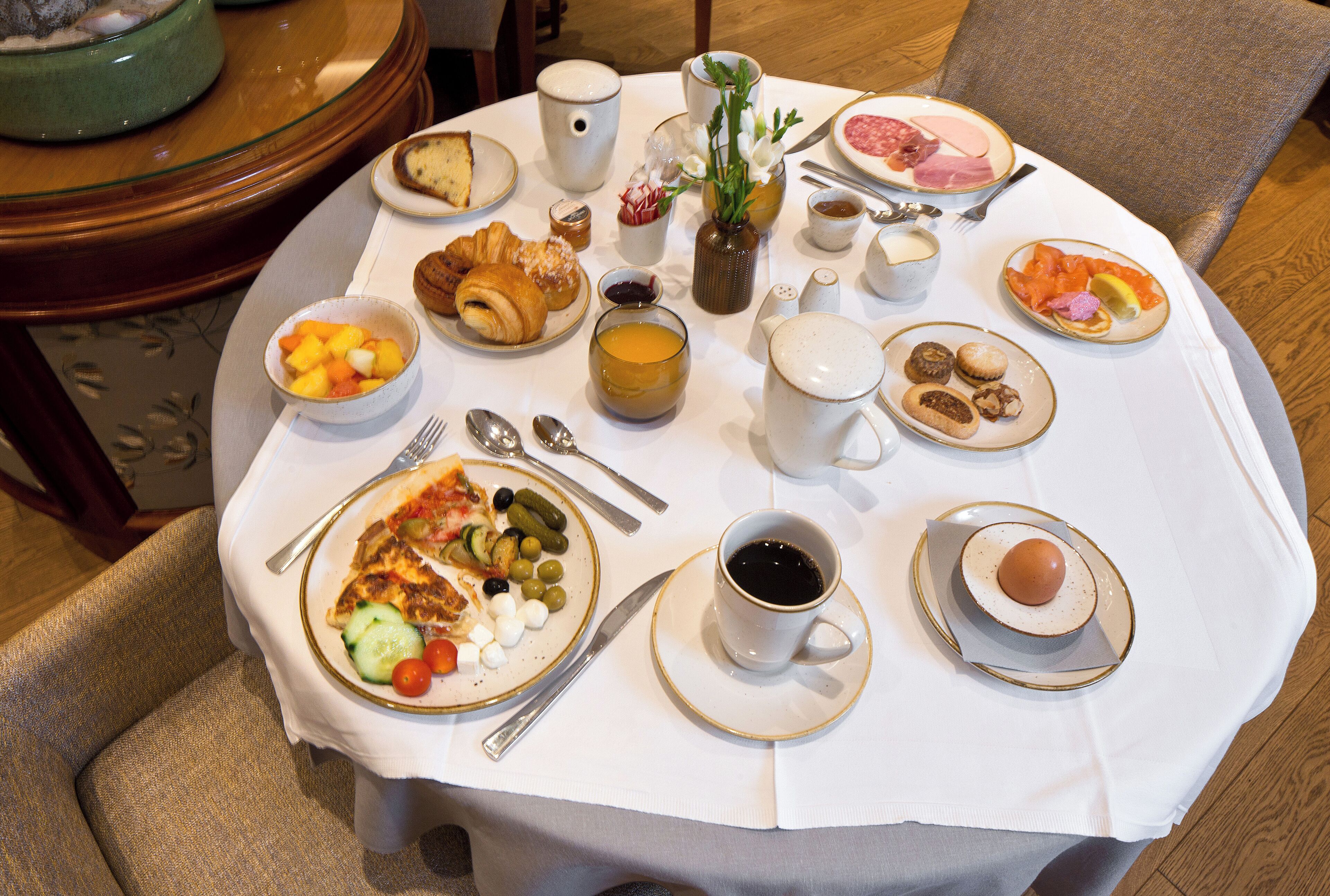 Una mesa de desayuno con diversos platos, como cruasanes, fruta y café.