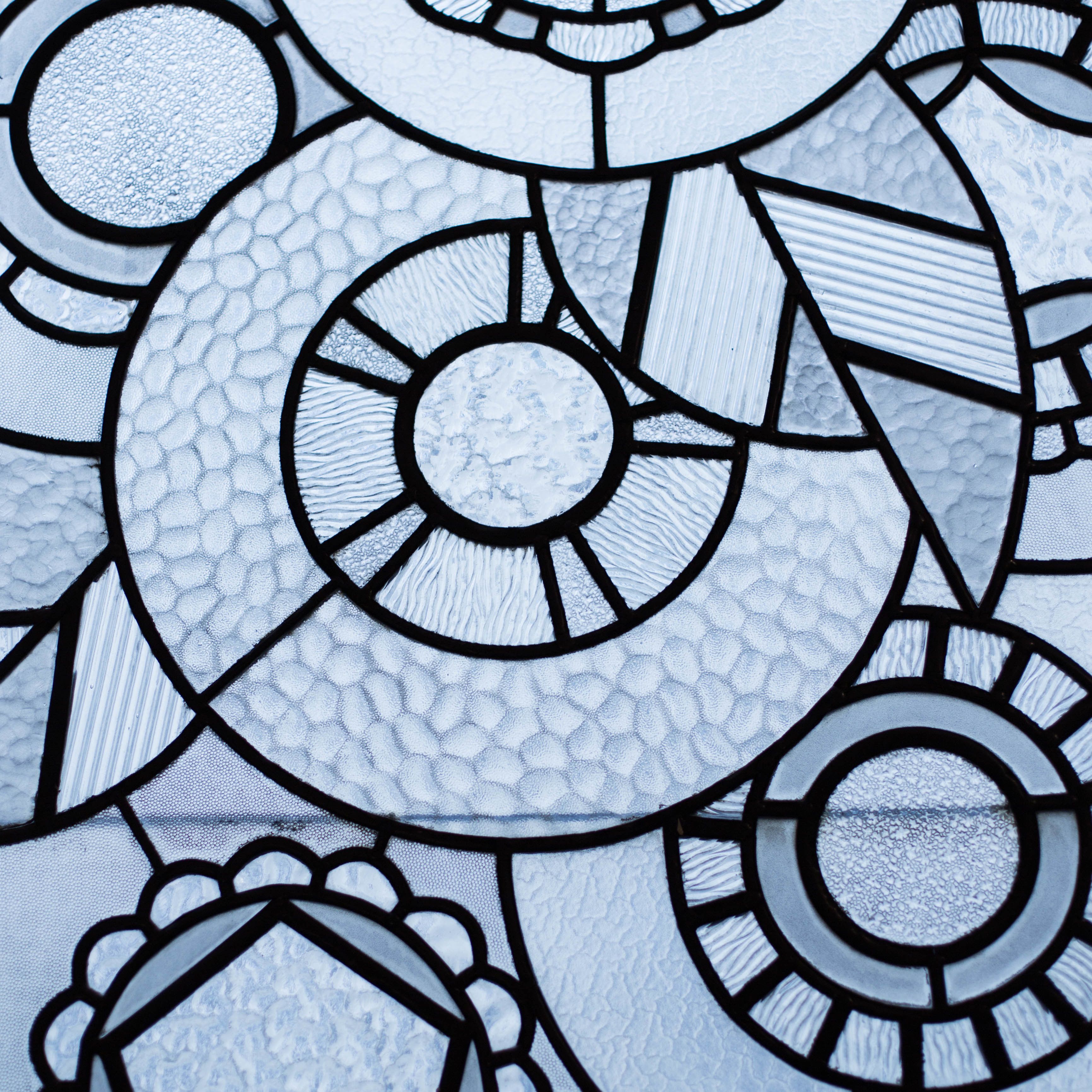 Un dettaglio di una vetrata istoriata con motivi geometrici e disegni circolari.