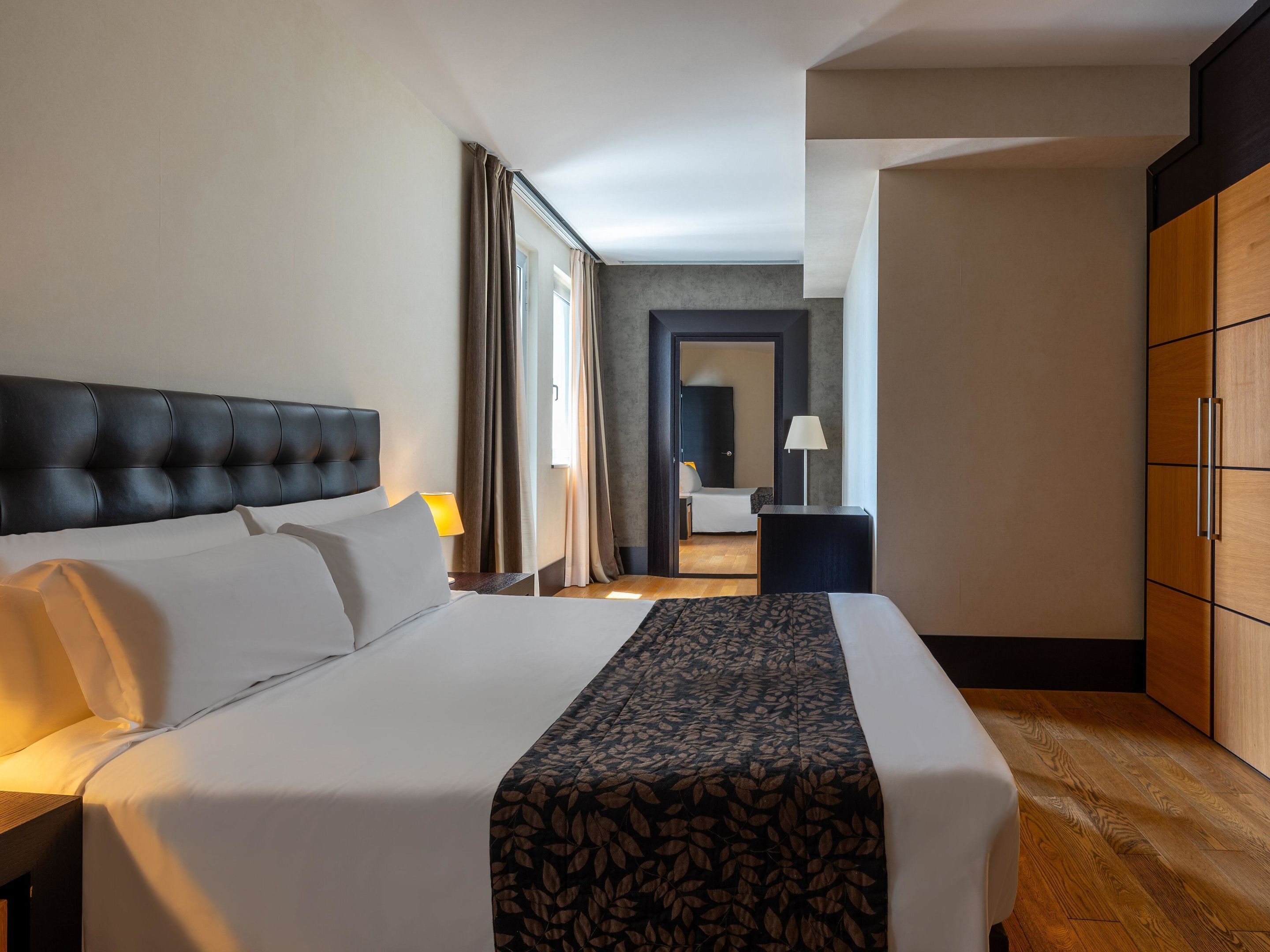 A hotel room with a large bed, a wardrobe, and a desk with a lamp.