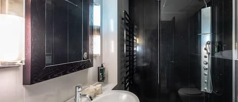 Un baño moderno con un espejo grande, un lavamanos blanco, una ducha con varios controles y un inodoro.