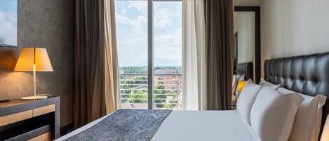 A hotel room with a large bed, a desk with a lamp, a view of the city through the window, and a cityscape visible outside.