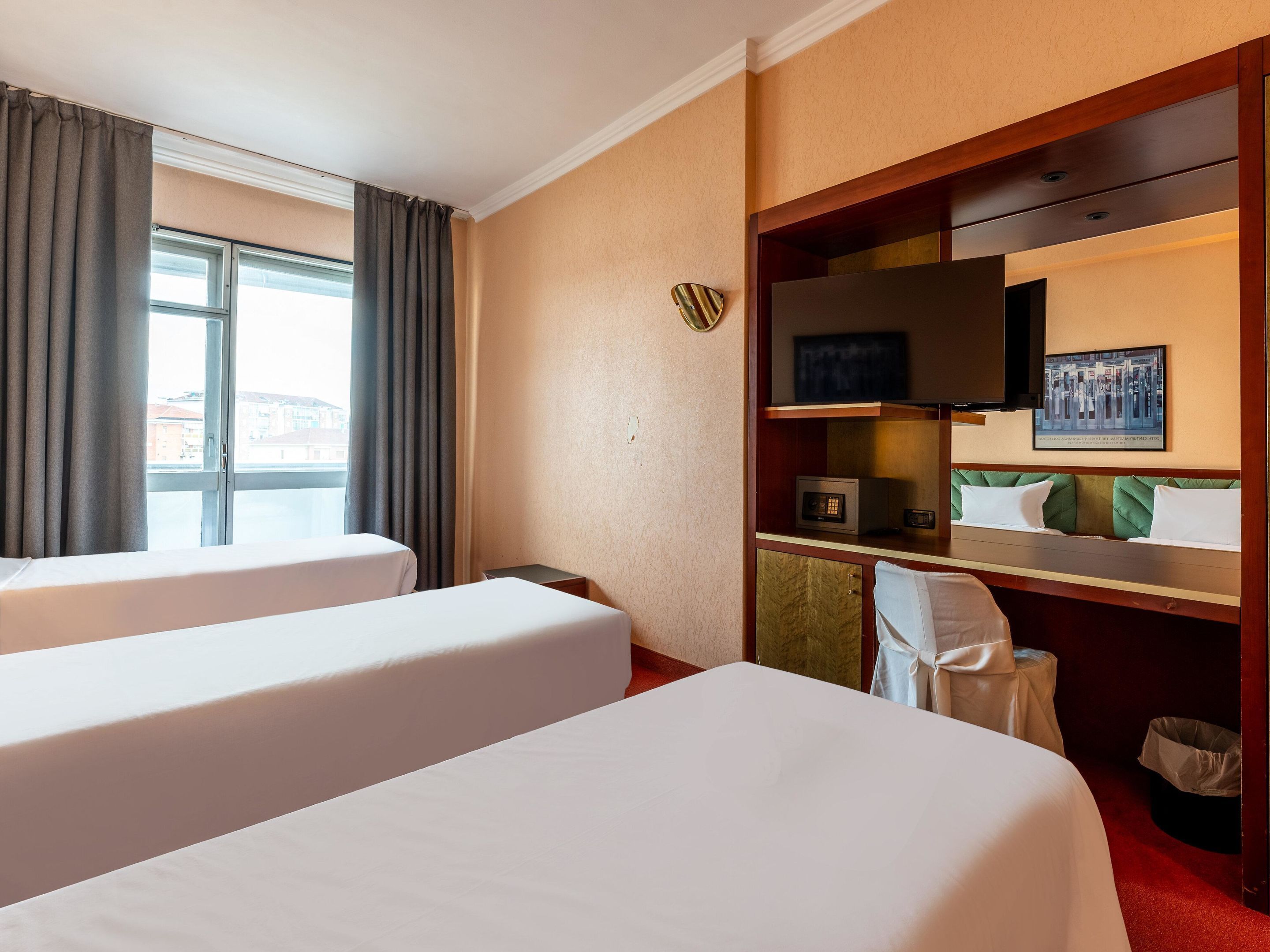 Ein Hotelzimmer mit zwei Betten, einem Schreibtisch mit Mikrowelle, einem Fernseher und einem Fenster mit Vorhängen.