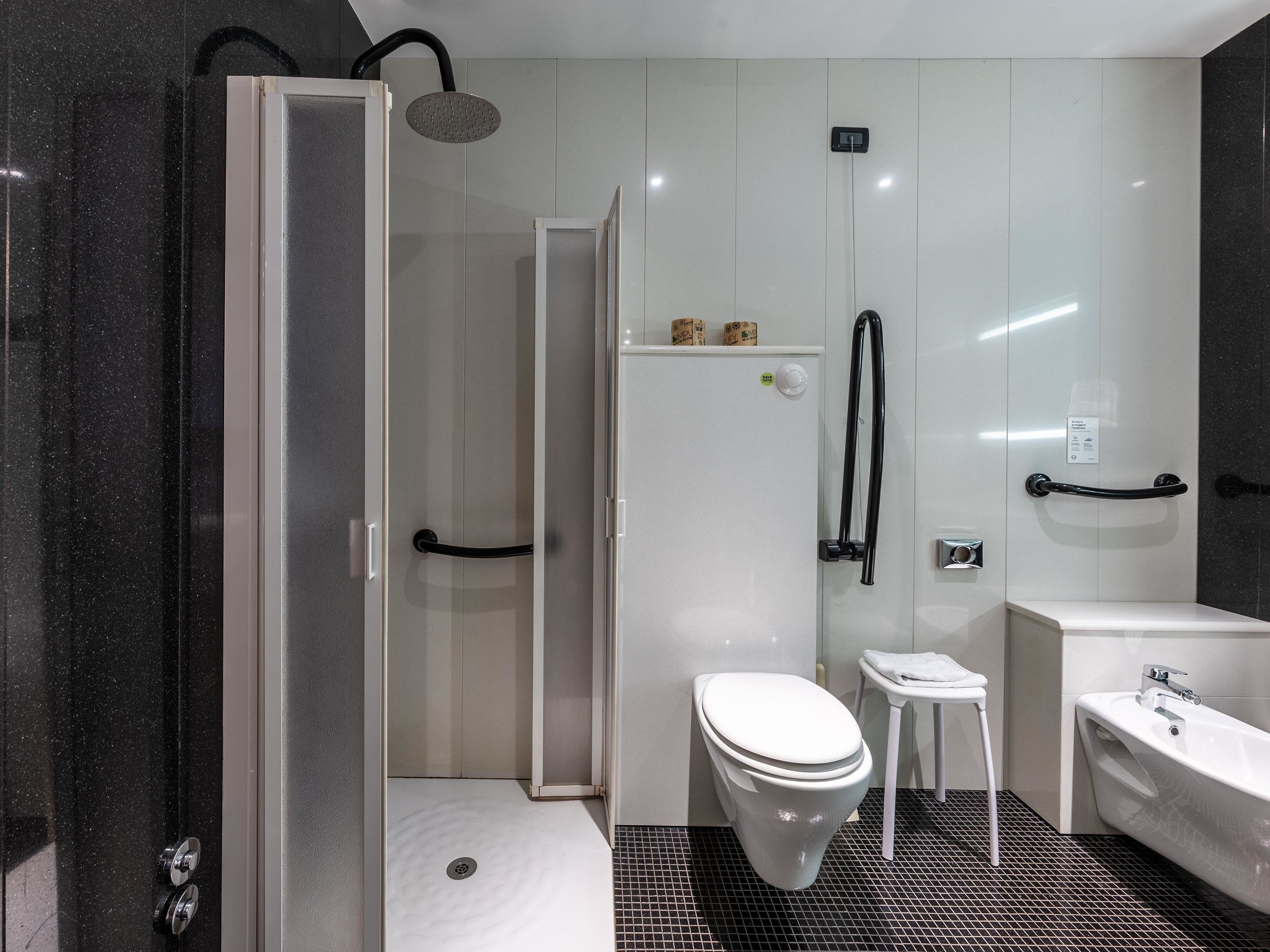 Une salle de bain moderne avec une douche à parois de verre, des toilettes blanches, un petit tabouret blanc et une baignoire sur pieds.