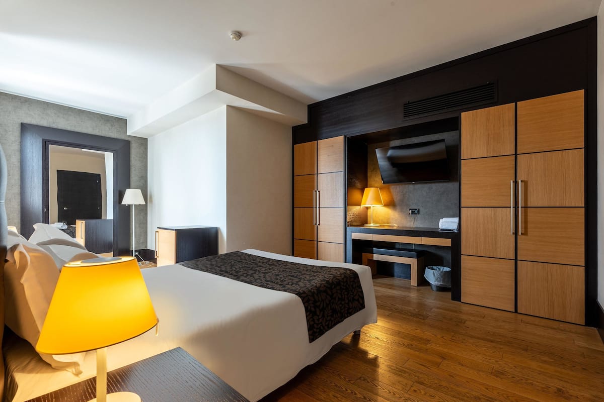 A modern hotel room with a large bed, a desk, and a wardrobe.