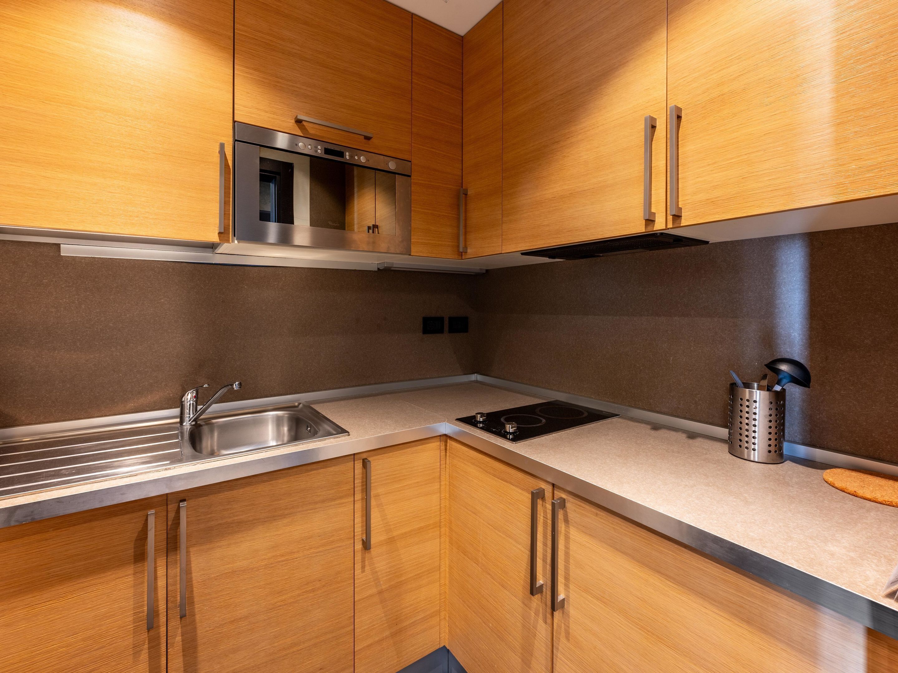 A modern kitchen with wooden cabinets, a stainless steel sink, a built-in oven, and a range hood.