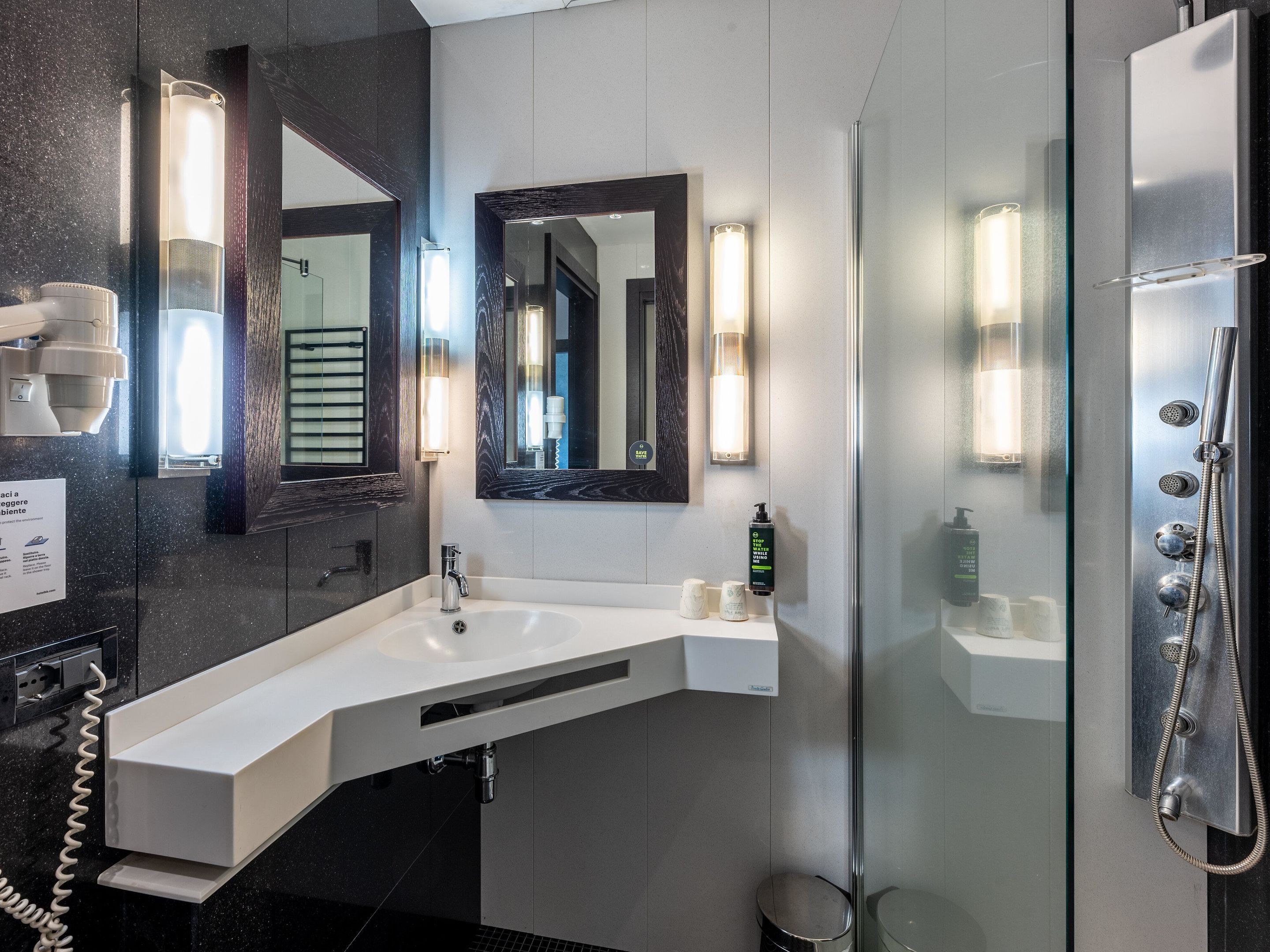 Une salle de bain moderne avec un grand miroir, un lavabo, une douche et un sèche-cheveux.