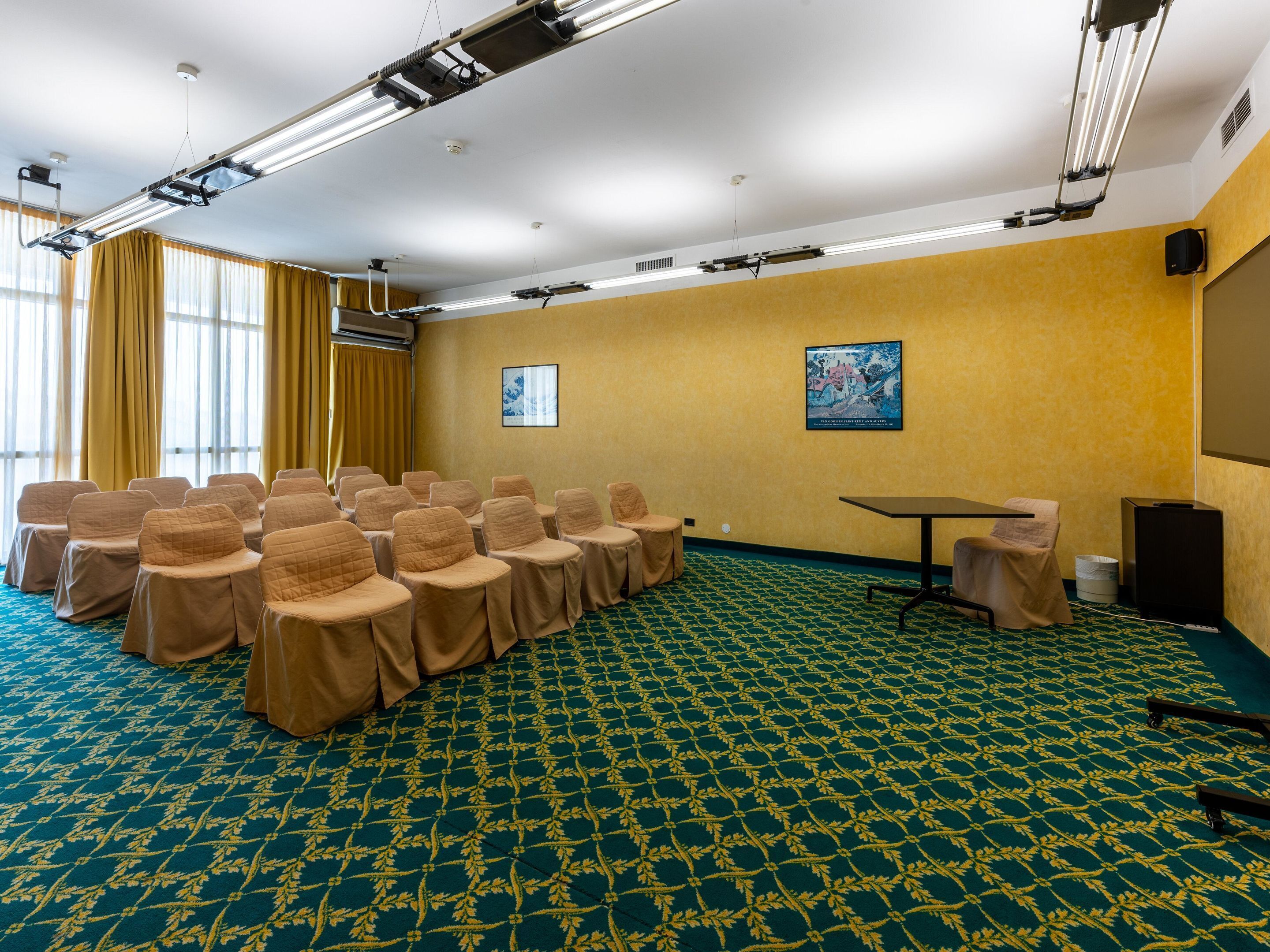 Un salón de conferencias con filas de sillas, un proyector y una pantalla en la pared.