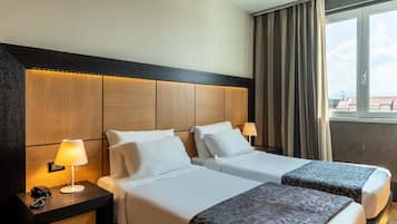 A hotel room with two beds, a wooden headboard, a nightstand with a lamp, and a window with curtains.
