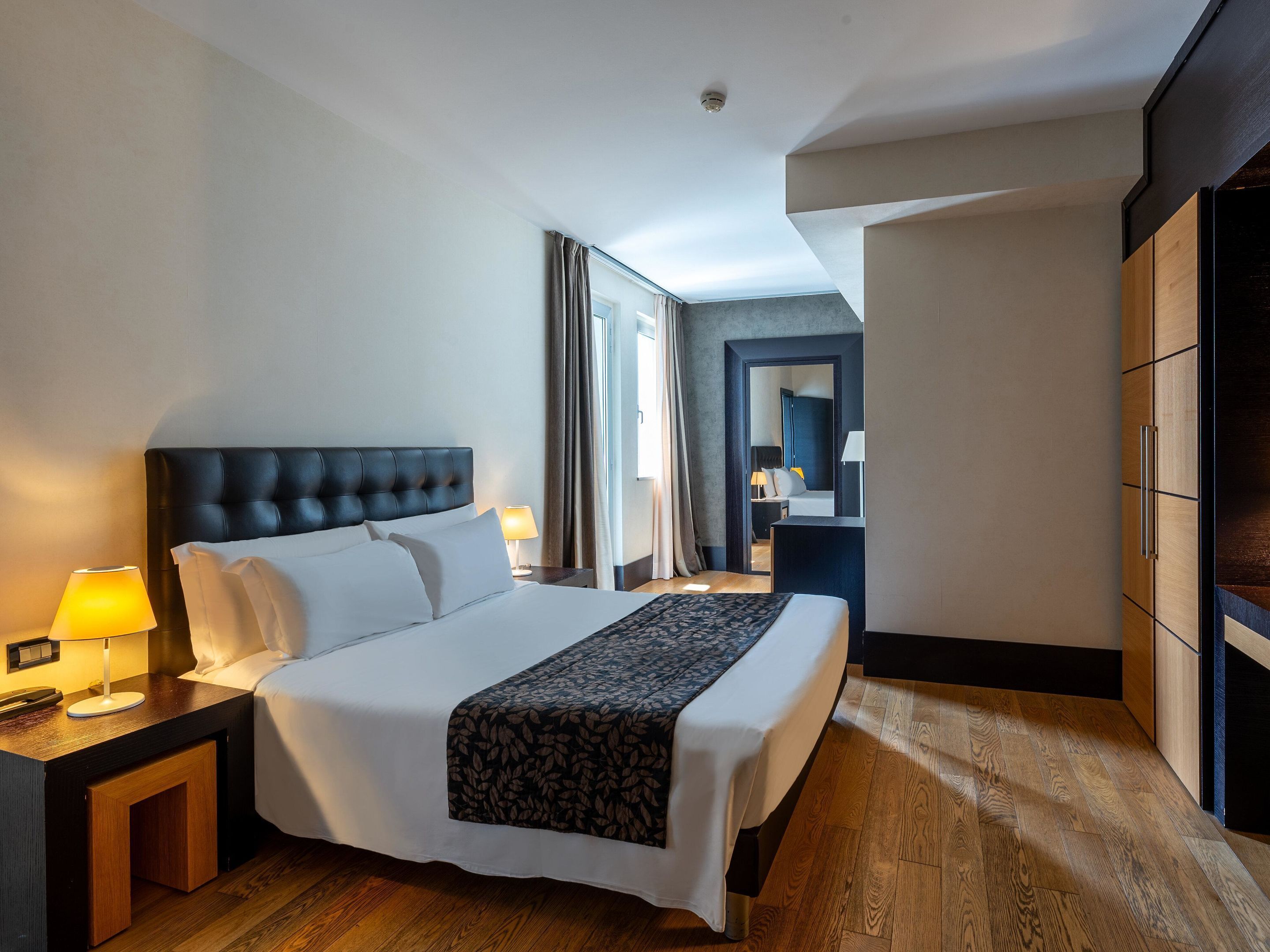 A hotel room with a large bed, bedside tables, a wardrobe, and a view of the hallway.
