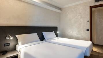 Een hotelkamer met twee eenpersoonsbedden, een nachtkastje met een lamp en een stopcontact.