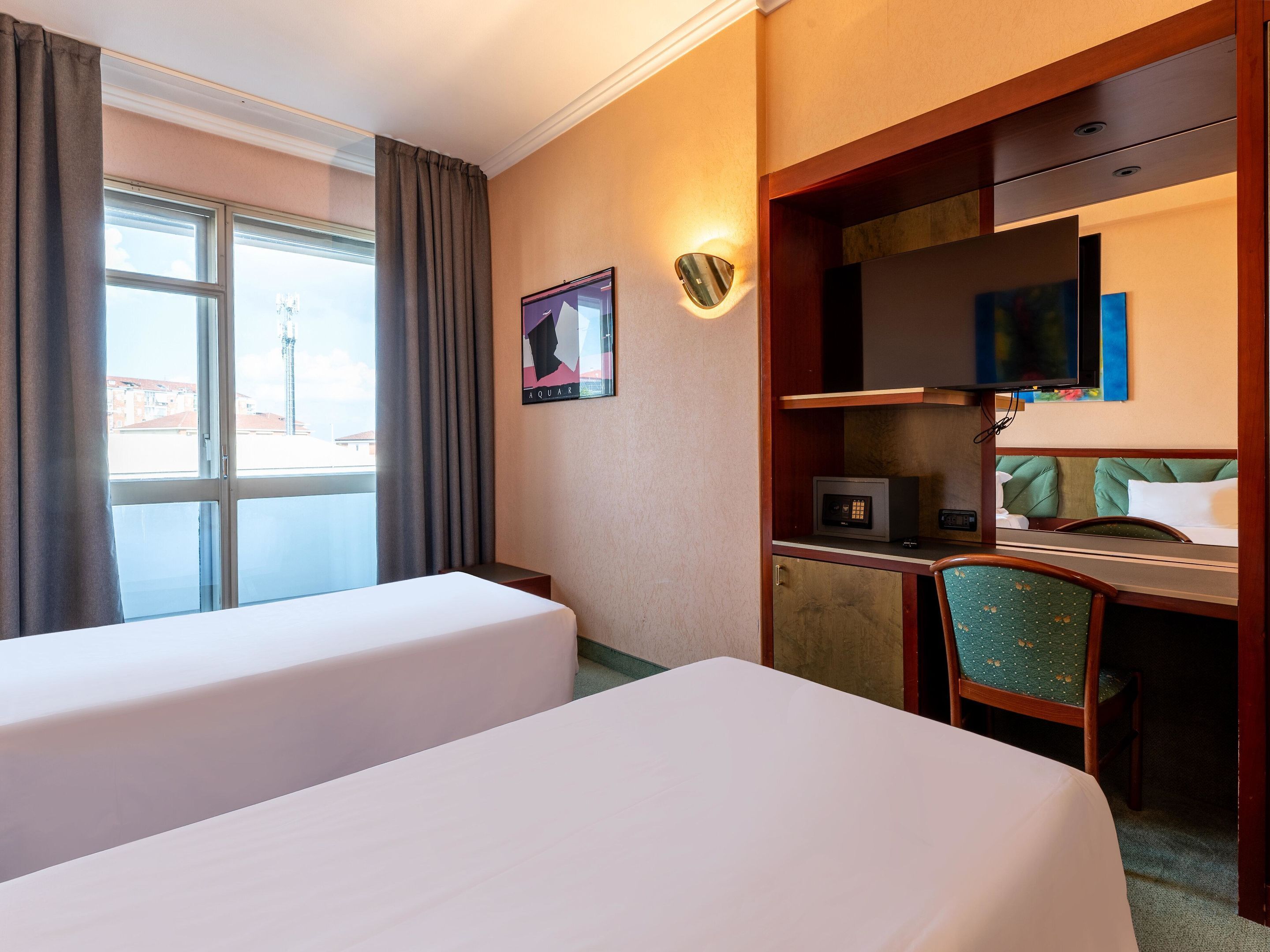 Une chambre d’hôtel avec deux lits, un bureau avec un ordinateur, une télévision et une fenêtre avec des rideaux.