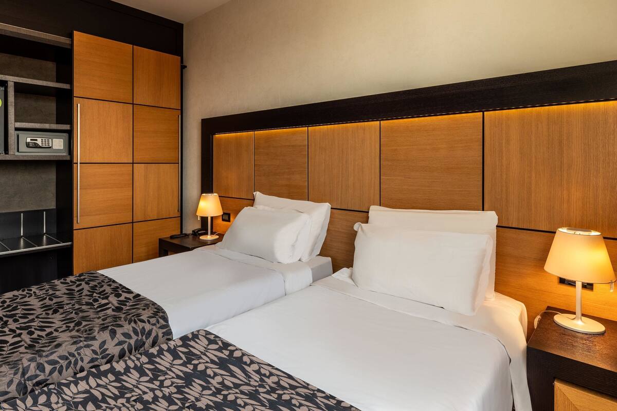 A hotel room with a large bed, two bedside tables, a built-in shelf with a microwave, and a headboard with integrated lighting.