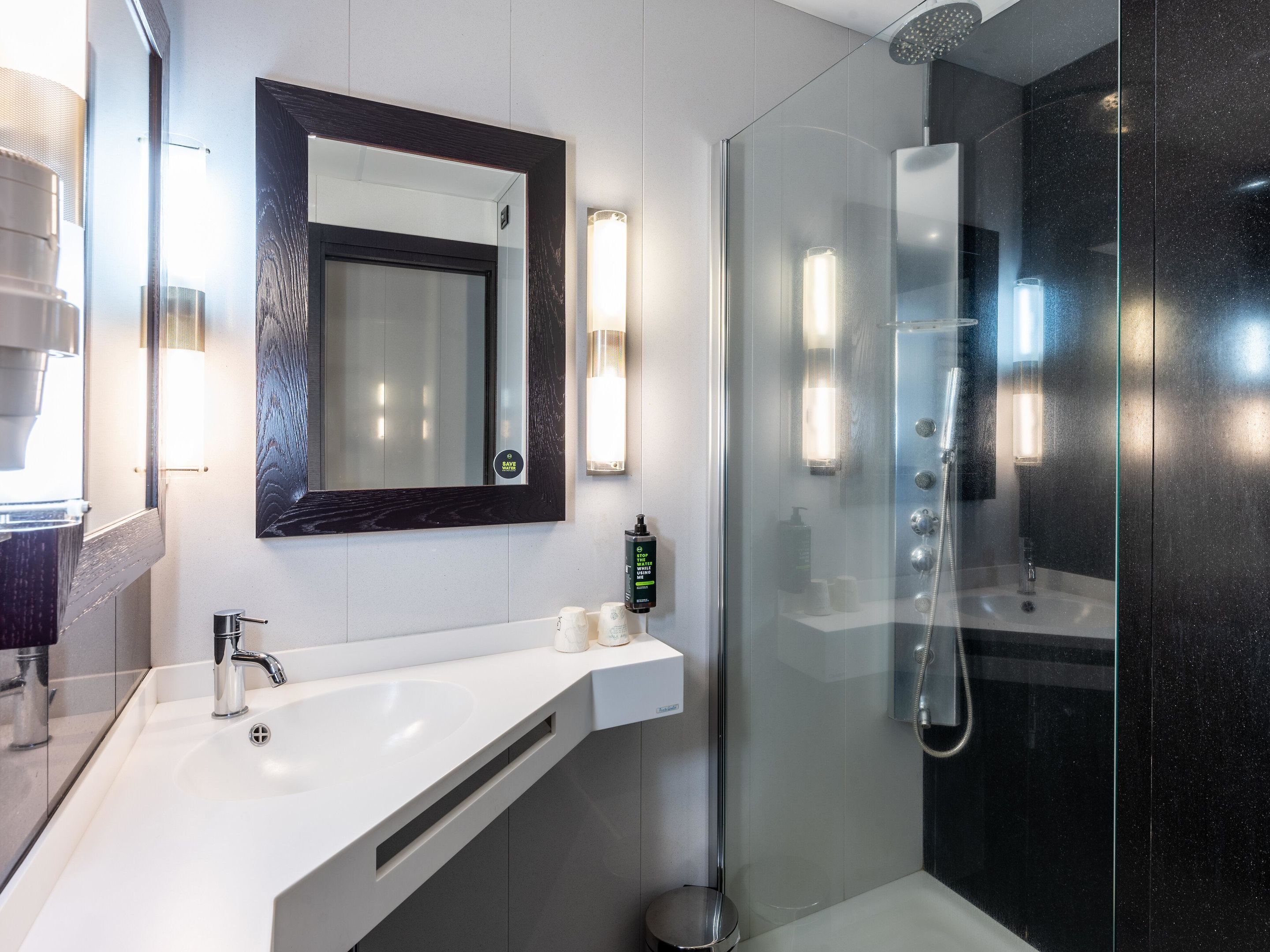 A modern bathroom with a white sink, a large mirror, a glass-enclosed shower, and wall-mounted lights.