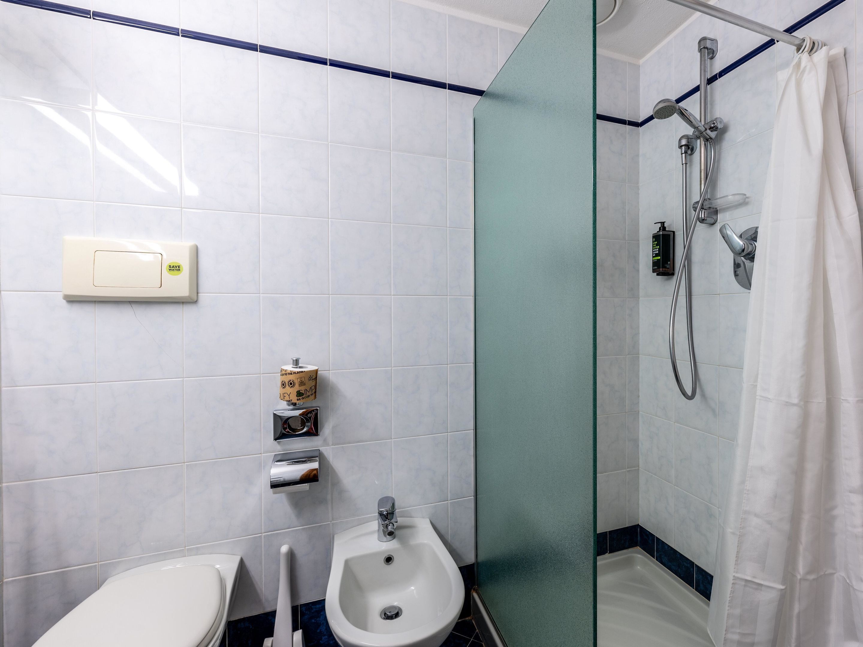A bathroom with white tiles, a bidet, a shower with a glass partition, and a towel rack.