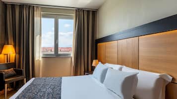 Een hotelkamer met een bed, een bureau, een stoel, een lamp en een raam met gordijnen.