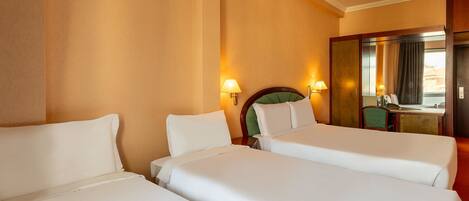 A hotel room with two single beds, a desk, a chair, a mirror, and two wall-mounted lamps.