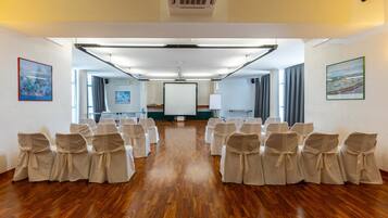 Un salón de conferencias con filas de sillas, una pantalla de proyector y una pizarra.