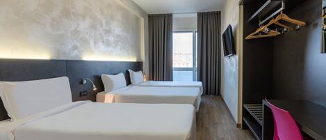 A hotel room with two beds, a desk, a TV, and a view of the city.