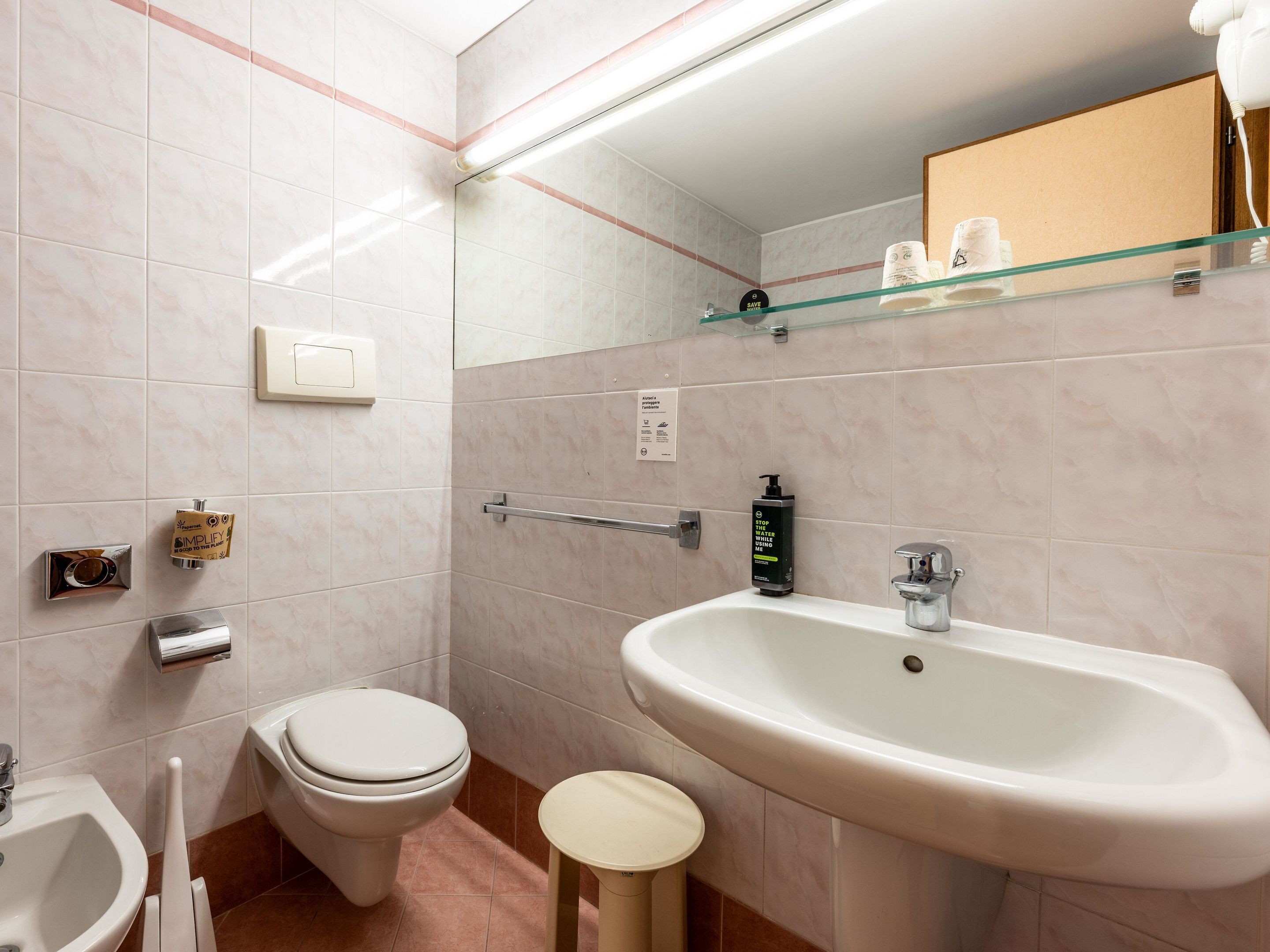 A modern bathroom with a toilet, bidet, sink, and glass shelf.